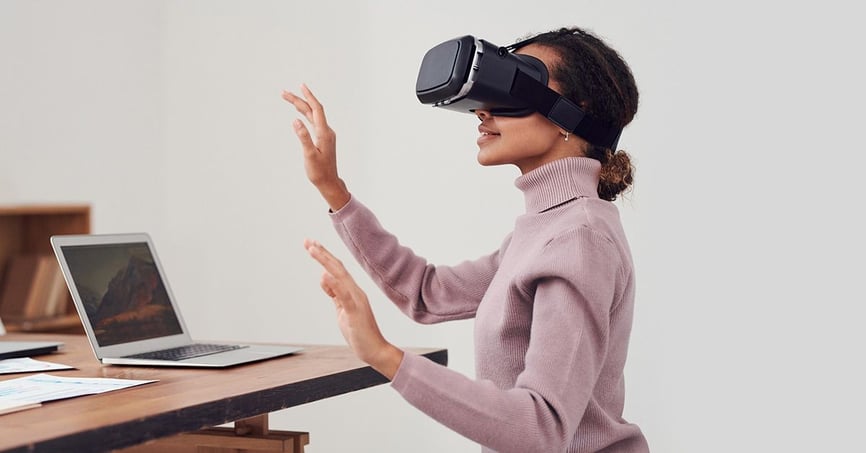 امرأة تستخدم سماعة رأس VR تجلس على مكتبها الذي يحتوي على ملاحظات وكمبيوتر محمول عليه