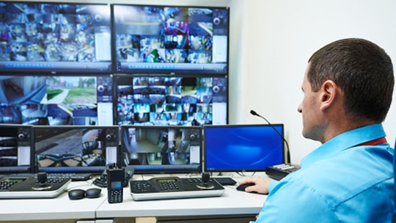 رجل في مركز التحكم الأمني في الحرم الجامعي يراقب الحرم الجامعي من خلال حائط فيديو يعرض لقطات الكاميرا الحية