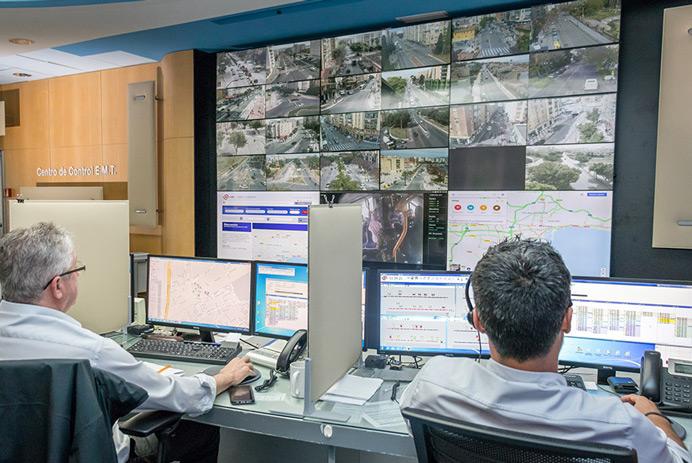  غرفة تحكم EMT Madrid مع عاملين يراقبان الطرق والبيانات المعروضة على حائط فيديو