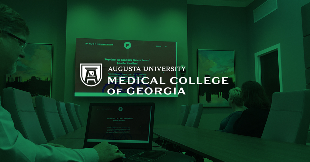 غرفة اجتماعات كلية الطب في جورجيا ، مع رجل يستخدم جهاز الكمبيوتر المحمول الخاص به و Userful لعرض صفحة ويب على حائط فيديو خلفه مع تراكب أخضر وشعار