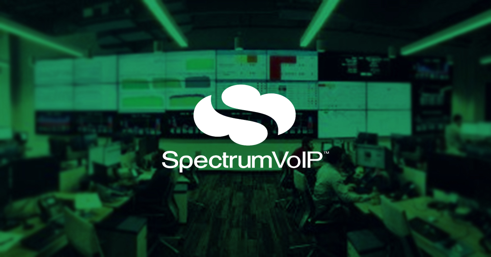 مركز عمليات شبكة SpectrumVoIP فارغ مع العديد من محطات العمل وجدار فيديو أكبر يعرض لوحات معلومات البيانات مع تراكب أخضر وشعار