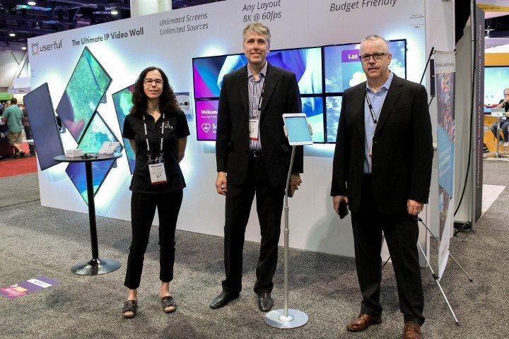 3 Userful employees at Infocomm 2018, in front of Userful AV-over-IP booth featuring a video wall