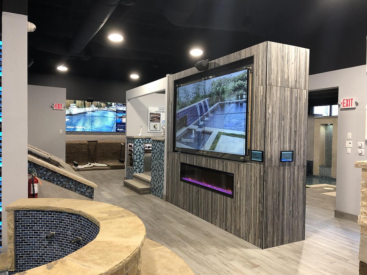 Pool showroom with modern standalone fireplace with built in video wall displaying pool advertisements