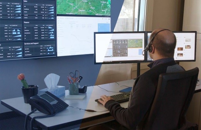 موظف في غرفة التحكم في مكتب عمله يكتب ، وينظر إلى حائط فيديو يعرض لوحات معلومات البيانات والخرائط