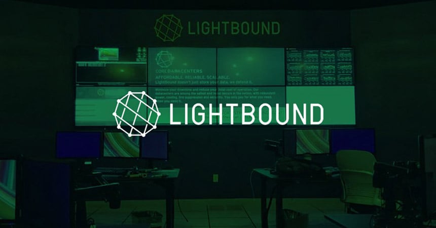 غرفة تحكم Lightbound فارغة مع 2 محطات عمل وجدار فيديو يعرض مواقع الويب والبيانات والإعلانات مع تراكب أخضر وشعار