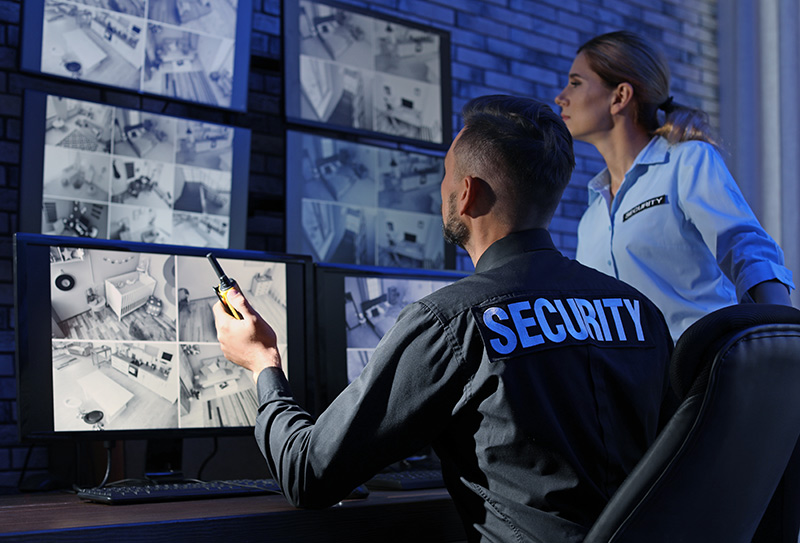 2 security guards monitor the inside of a building through live camera footage on a video wall